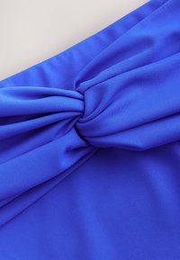 Jasnoniebieska tkanina skręcona w węzeł, ukazująca fakturę i fałdy na jasnym tle.