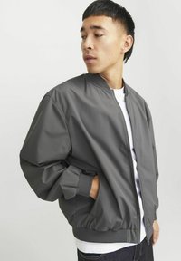 Gray bomber jacket with a zip front, ribbed cuffs, and waistband. Made of smooth fabric, featuring a relaxed fit and side pockets.