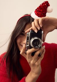 Vintage camera with black body and silver accents held by a person wearing a fluffy red sweater and a red sequined Santa hat.