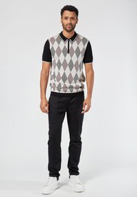 Lyhythihaisessa argyle-neulepuserossa on kerma, mustia ja punaisia timanttikuvioita. Se on yhdistetty mustiin housuihin ja valkoisiin lenkkarit.