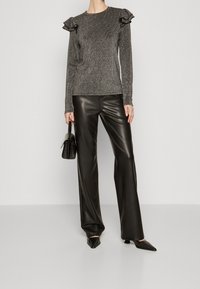 Top grigio metallico a maniche lunghe con dettagli a ruffle sulle spalle, abbinato a pantaloni neri in ecopelle a vita alta e tacchi neri a punta.