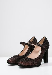 Chaussures Mary Jane à talons hauts noires en sequins, avec un bout fermé et une sangle ajustable, présentant une surface texturée et un talon épais.