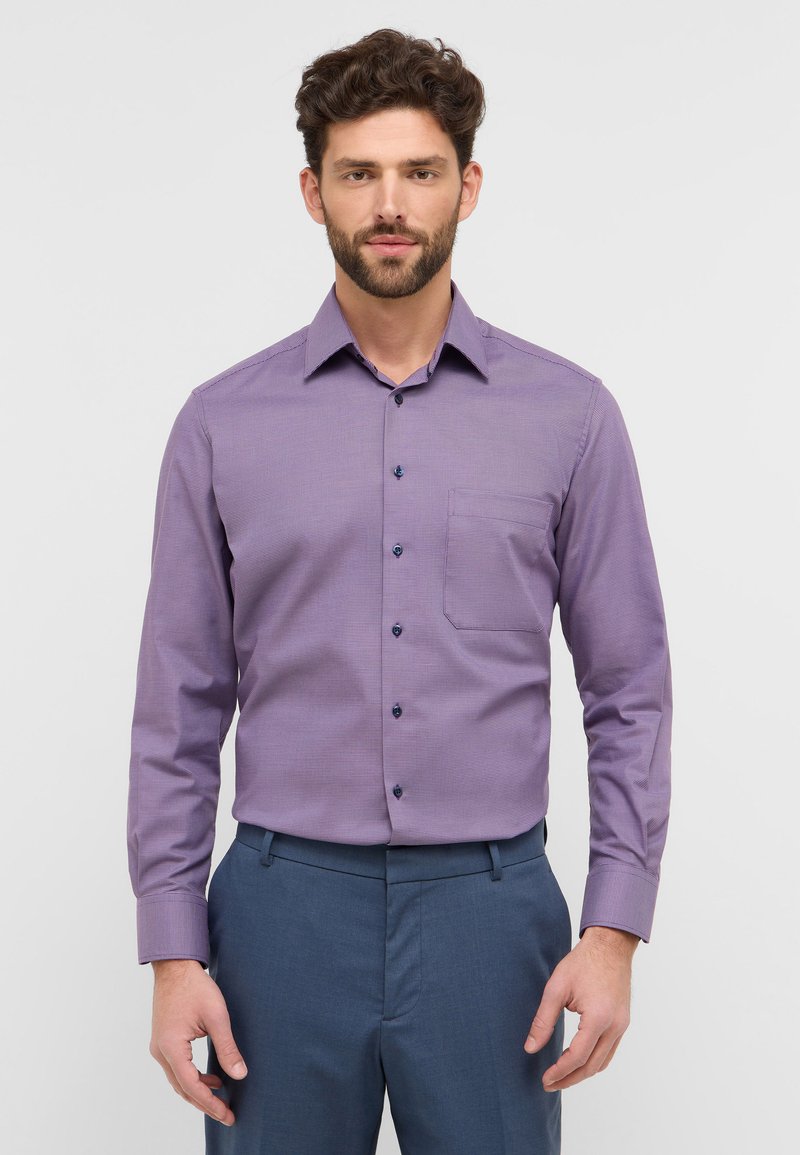 Lila karierte Hemdbluse mit langen Ärmeln und einem button-down Kragen, ausgestattet mit dunklen Knöpfen und einer Brusttasche, kombiniert mit blauen Hosen.