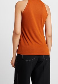 Top naranja con canalones y un diseño ajustado. La espalda tiene un corte bajo y no presenta logotipos visibles. Combinado con pantalones negros holgados.