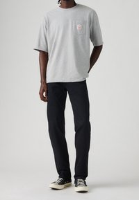 Camiseta gris de algodón con mangas cortas y un bolsillo en el pecho, combinada con pantalones negros y zapatillas negras con cordones y suelas blancas.