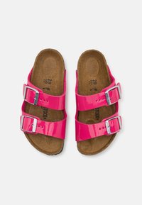 Sandali in pelle sintetica rosa lucida con due fibbie regolabili, soletta in sughero e una soletta interna testurizzata, caratterizzati da un design piatto e da uno stile aperto davanti.