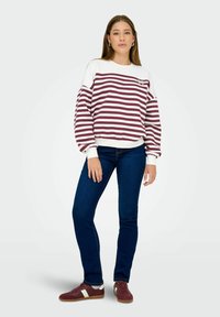 Márkovaná mikina v bordó a bílé pruhy s kulatým výstřihem a volným střihem. Spárovaná s tmavě modrými slim-fit džíny a vínovými teniskami.