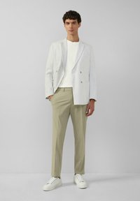 Hellgrau doppelt geknöpfter Blazer, cremefarbenes T-Shirt, olivgrüne Hose und weiße Sneakers. Glatte Texturen und taillierte Passform.