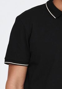 Schwarzes Polo-Shirt mit kurzen Ärmeln, ausgestattet mit einem weißen Kragen und Ärmelschneidern. Hergestellt aus glattem Stoff mit klassischer Passform.