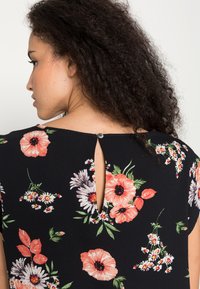 Top preto floral com flores rosa e brancas, mangas curtas e um acabamento nas costas em forma de olho de fechadura com fecho de botão. Textura suave e corte descontraído.