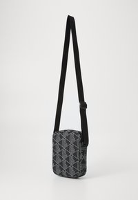 Borsa a tracolla nera e grigia con motivo geometrico e spallaccio regolabile nero su uno sfondo bianco semplice.