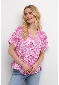 Blusa a maniche corte di colore rosa con motivo floreale, dotata di bottoni sul davanti, caratterizzata da un taglio morbido e un tessuto leggero. L'orlo ondulato aggiunge un tocco di eleganza.