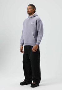 Lavendelkleurige hoodie met een kangoeroezak, geribbelde manchetten en een geborduurd logo, gecombineerd met zwarte wijde jeans en zwarte schoenen met roze veters.