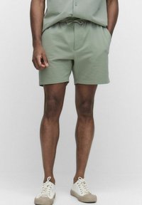 Grønne teksturerede shorts med elastisk talje og snøre. Har sidelommer og er parret med hvide sneaks.