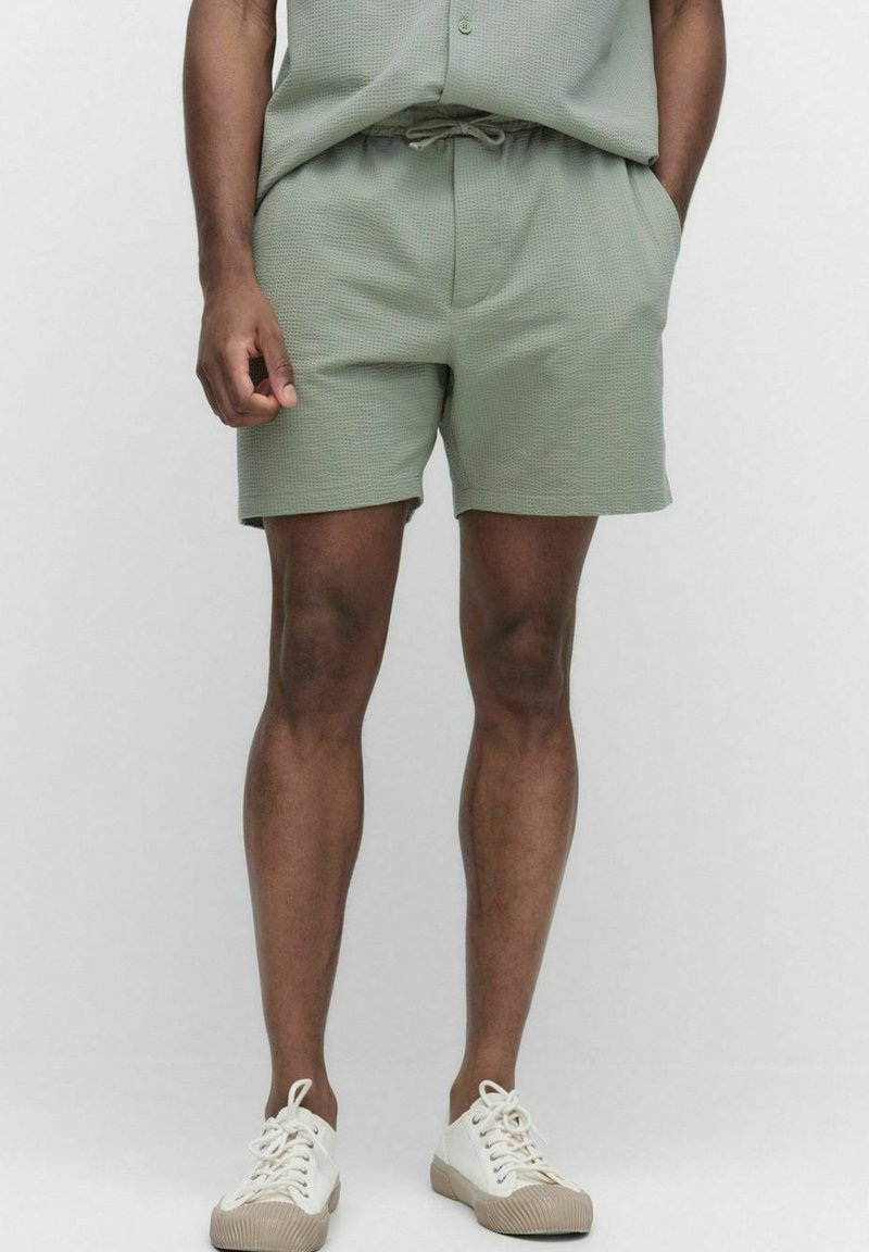 Grønne teksturerede shorts med elastisk talje og snøre. Har sidelommer og er parret med hvide sneaks.