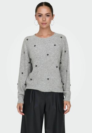 Suéter de lana gris claro con cuello redondo, mangas largas y adornos florales negros. Combinado con pantalones negros de corte holgado.