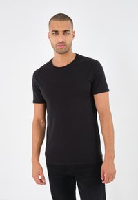 Schwarzes kurzärmliges T-Shirt aus Baumwolle mit rundem Halsausschnitt. Glatte Textur mit klassischem Schnitt, kombiniert mit dunklen Hosen.