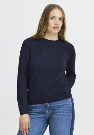 Mørkeblå striktrøje med rund halsudskæring og lange ærmer, der har en glat tekstur samt ribkant ved ærmerne og i kanten. Kombinationen med blå jeans.