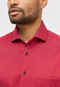 Rotes, gewebtes Hemd mit Button-Down-Kragen, ausgestattet mit marineblauen Knöpfen und einem karierten Muster im Kragen. Mit einer Brusttasche.