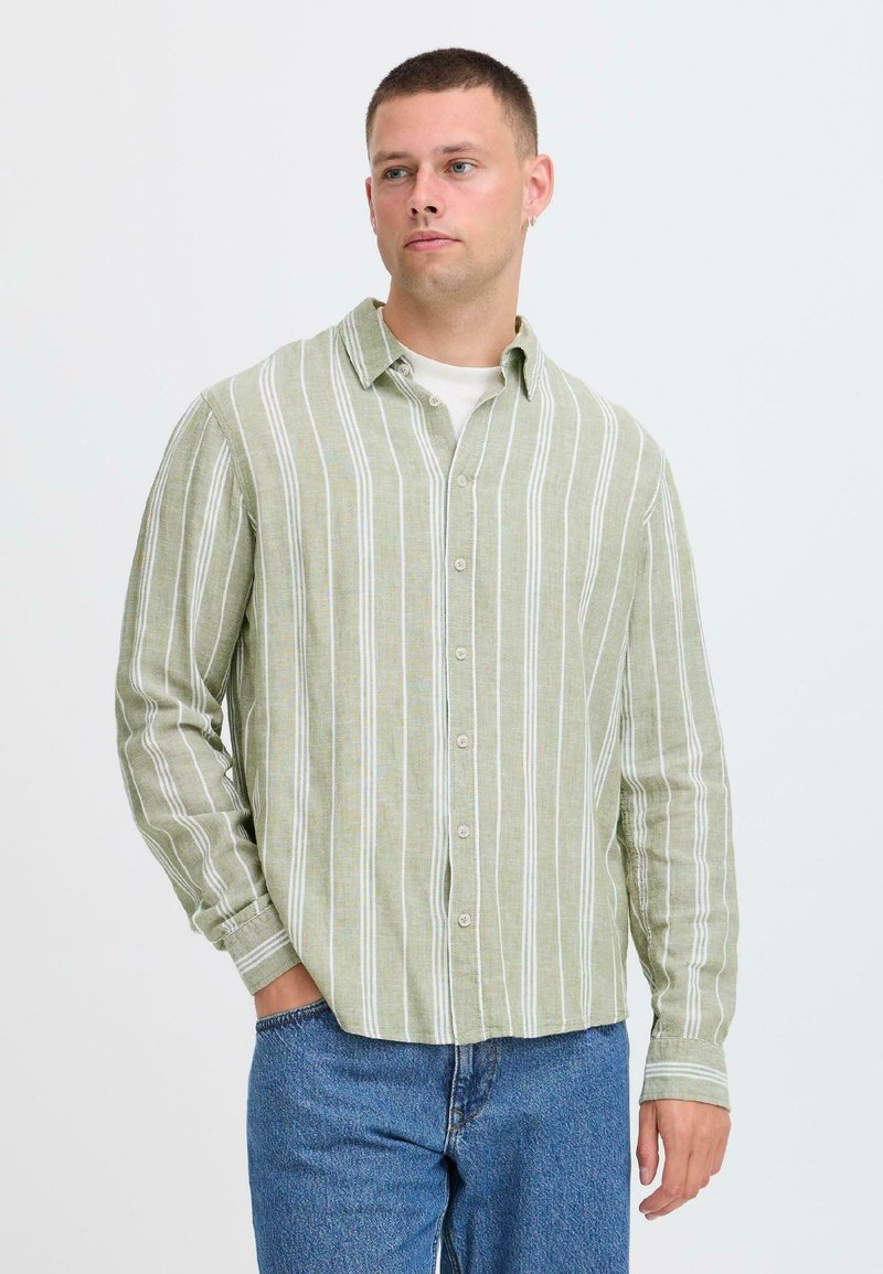 Chemise à rayures vertes avec des rayures blanches, manches longues, coupe décontractée et col, associée à un jean en denim bleu.