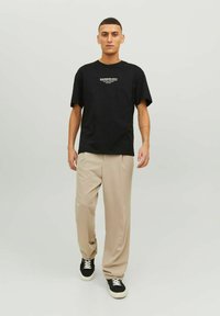 Must musta T-särk valgete kirjadega, millele on sobitatud beežid vabalt langetavad püksid ja mustad tossud. Sirge lõikega, lõdva disainiga.