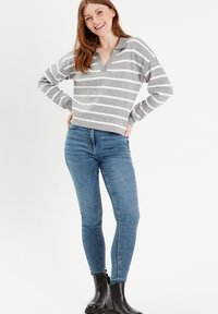 Grå og hvid stribet sweater med V-hals og krave, parret med blå skinny jeans og sorte ankelstøvler.