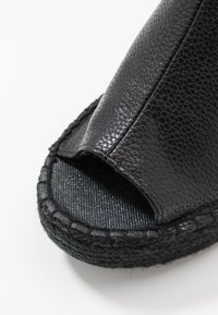 Sandalia deslizante de cuero negro con parte superior texturizada, punta abierta y suela negra trenzada. Presenta un detalle cosido alrededor de los bordes.