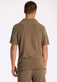 Korte mouw colbert shirt gemaakt van gestructureerde bruin stof. Bevat een ontspannen pasvorm en zijsplitten. Achteraan ziet het er glad uit.