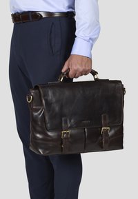 Brown leather briefcase with a front flap, two buckles, and top handle. Smooth texture, rectangular shape, and gold-tone hardware accents.