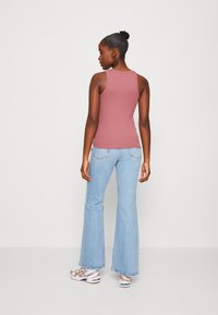 Top sin mangas rosa ajustado, combinado con jeans acampanados de color azul claro. El atuendo se complementa con zapatillas plateadas y rojas. Diseño simple y casual.