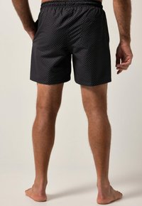 Schwarze Badeshorts mit einem Diamantenmuster, elastischem Bund, seitlichen Taschen und einem Schnitt bis zur Mitte des Oberschenkels. Glatte Textur, leichtes Material.