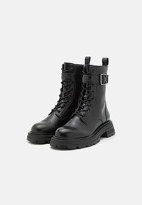 Botas de tobillo de cuero negro con punta redondeada, cordones en la parte frontal, correa ajustable con hebilla y suela de goma texturizada.