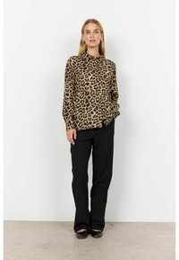 Blůza s leopardím potiskem v hnědé a černé barvě, dlouhé rukávy, zapínání na knoflíky. Spárovaná s černými kalhotami a plochými botami. Jednoduché pozadí.
