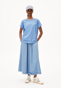 Hellblaues kurzärmliges Oberteil kombiniert mit einem Denim-Maxikragen; hat eine lockere Passform. Akzentuiert mit weißen atmungsaktiven Schuhen und einer passenden Kappe.