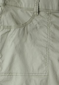 Närbild av ljusgrön tyg med en sydd ficka, synliga sömmar och en lätt krusad textur.