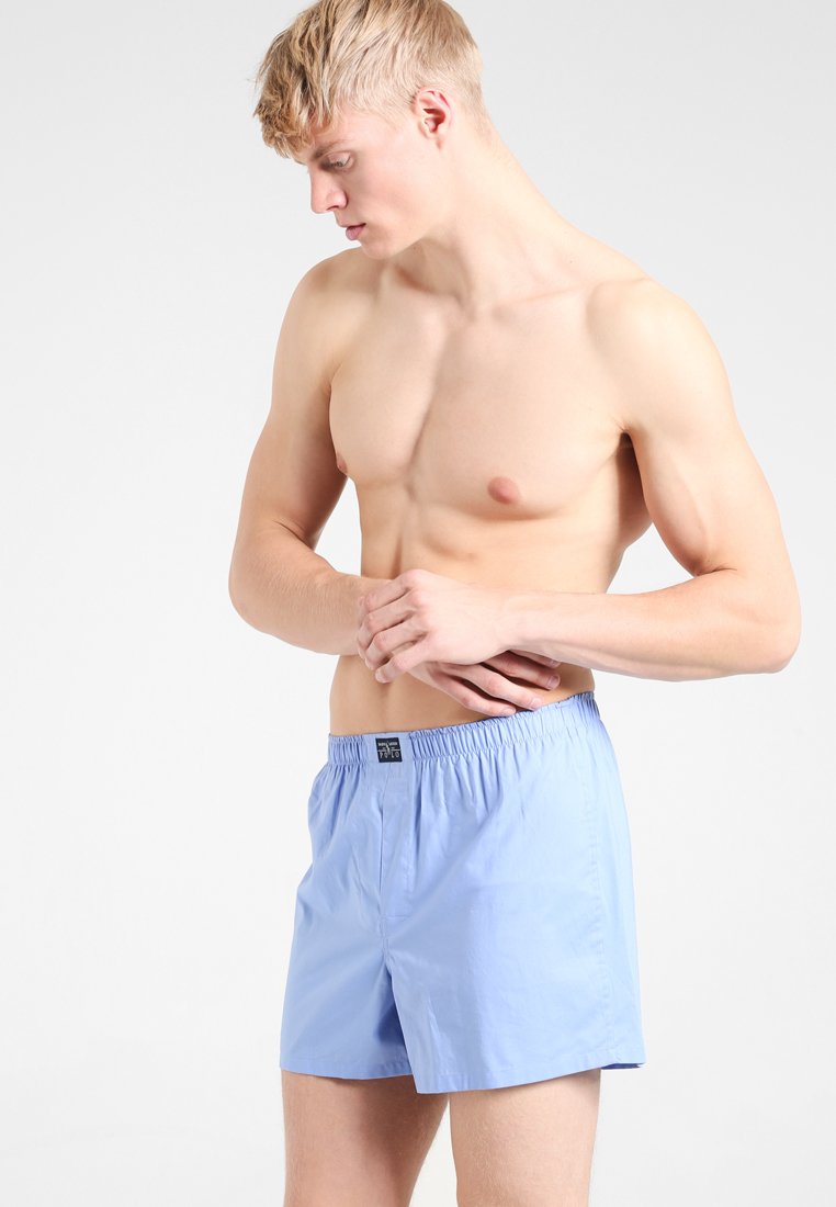 Lichtblauwe katoenen shorts met een elastische tailleband. Eenvoudig design, knielang en een gladde textuur, met een klein label op de tailleband.