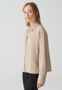 Beige overhemdo met kraag, lange mouwen, zijzakken en een relaxte pasvorm. Gladde stof met subtiele textuurcontrasten.