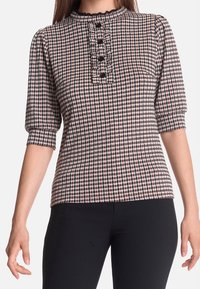 Svartvit hundtandsmönstrad topp med hög halsringning. Har puffade ärmar, en texturerad yta och fyra svarta knappar framtill.