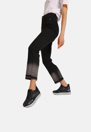 Jeans neri a vita alta con orlo sbiadito abbinati a sneakers nere con suola bianca e dettagli in argento. Materiale morbido, vestibilità casual.