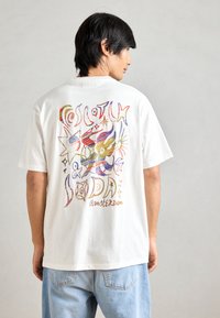 Λευκό βαμβακερό T-shirt με μια πολύχρωμη γραφική απεικόνιση στην πλάτη, περιλαμβάνοντας καλλιτεχνικό κείμενο και αφηρημένα σχέδια. Κ Casual, άνετη εφαρμογή.