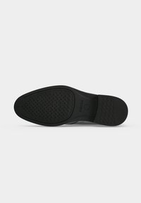 Semelle en caoutchouc noir d'une chaussure habillée avec des motifs de grip texturés et le logo GEOX embossé près de la zone de la voûte plantaire.