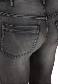 Gros plan sur l'arrière d'un jean en denim gris foncé montrant les coutures, les passants de ceinture et deux poches arrière.