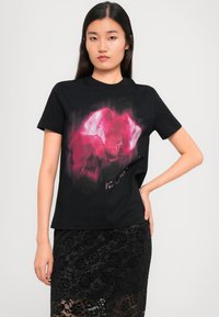 Black cotton t-shirt featuring a prominent graphic in shades of pink and purple, with short sleeves and round neckline, paired with a black lace skirt.