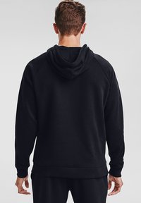 Felpa nera con una texture liscia, dotata di un ampio cappuccio, polsini a coste e un orlo a coste. Il design include maniche raglan.