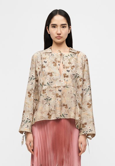 Μπεζ μπλούζα με λουλουδάτο μοτίβο, ντεκολτέ με άνοιγμα σε σχήμα κλειδαρότρυπας, άνετη εφαρμογή και μακριά μανίκια με κορδόνια στα μανσέτα. Μαλακό, ελαφρύ ύφασμα.