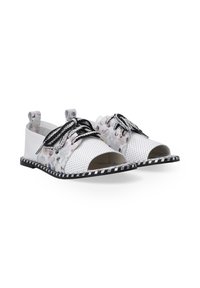 Gesloten schoenen van witte geperforeerd materiaal met bloemenpatroon en zwarte veters, met een zwart-wit gestreepte zool.