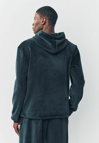 Felpa con cappuccio di un verde scuro in tessuto morbido e texturizzato, caratterizzata da una vestibilità rilassata e dettagli a coste sui polsini e sull'orlo.
