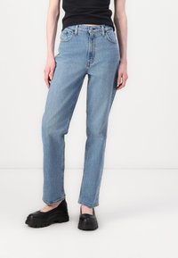 Jean droit bleu clair en denim, avec un design classique à cinq poches, des passants de ceinture et une fermeture à bouton.