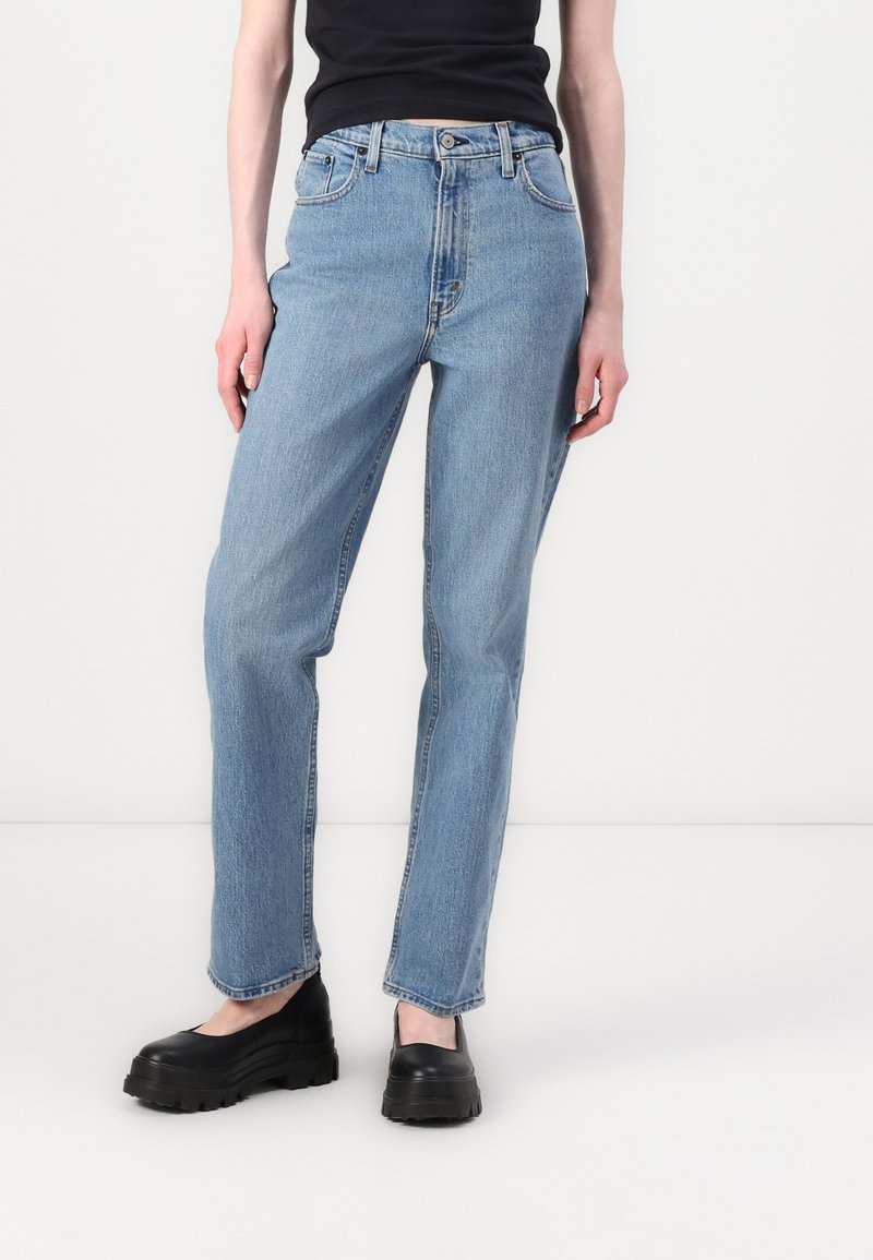 Jean droit bleu clair en denim, avec un design classique à cinq poches, des passants de ceinture et une fermeture à bouton.