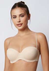 Reggiseno imbottito beige con ferretto, coppe senza cuciture e spalline sottili regolabili. Il tessuto è liscio con dettagli di cucitura sottili.